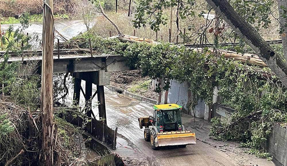 A tractor clears mud beneath a storm-damaged rail bridge covered with fallen trees near New Brighton.
