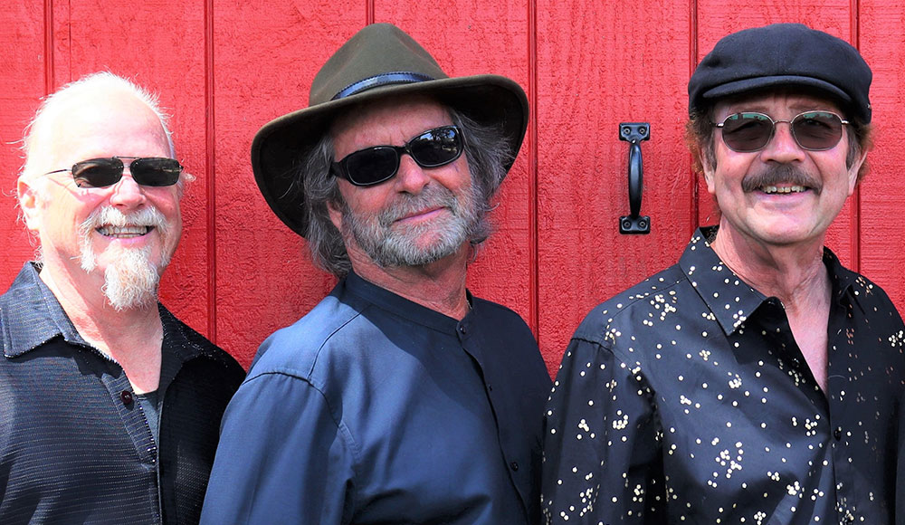 Original members of Santa Cruz rock band Snail standing together against a red wall