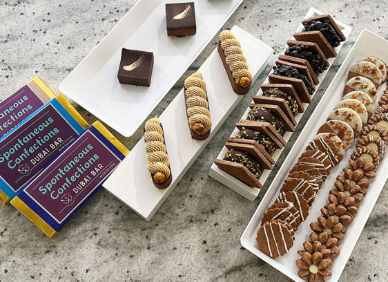 Pastry Prowess An assortment of Spontaneous Confections pastries and desserts arranged on white platters, including Dubai bars, brownies, tarts, and cookies.