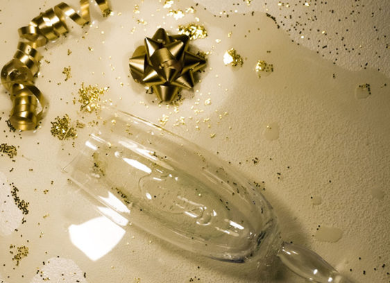 Toasting Moderation Broken champagne flute surrounded by gold ribbon and glitter on a white surface, symbolizing the aftermath of holiday overindulgence.