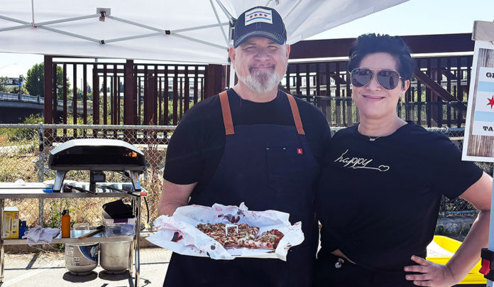 Sunflower Soul J.R. Chapman and Viviana of Girasol Pizza hold a Chicago-style thin-crust pizza at a pop-up food setup.