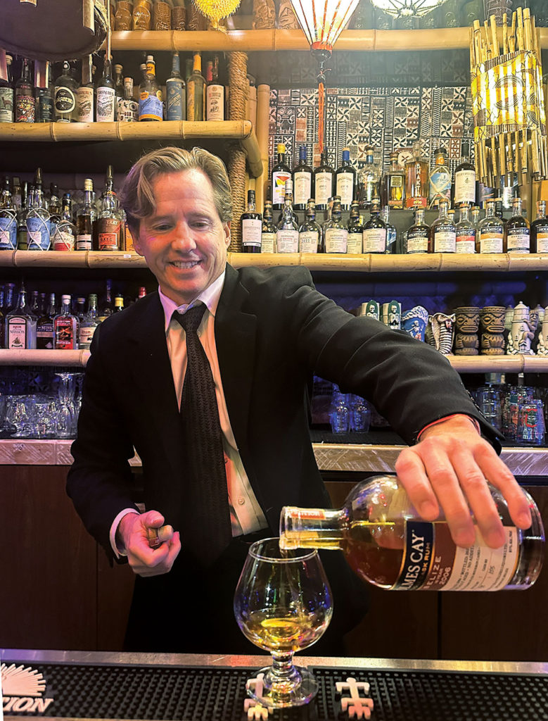 Man at a bar, pouring liquid from a liquor bottle into a glass