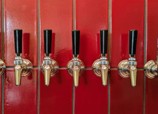 Level-Up Liquids A row of polished beer taps mounted against a glossy red tile wall inside Other Brother Beer Co.