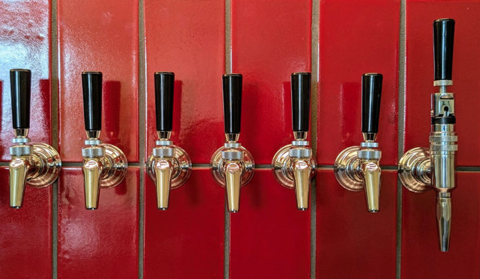 Level-Up Liquids A row of polished beer taps mounted against a glossy red tile wall inside Other Brother Beer Co.