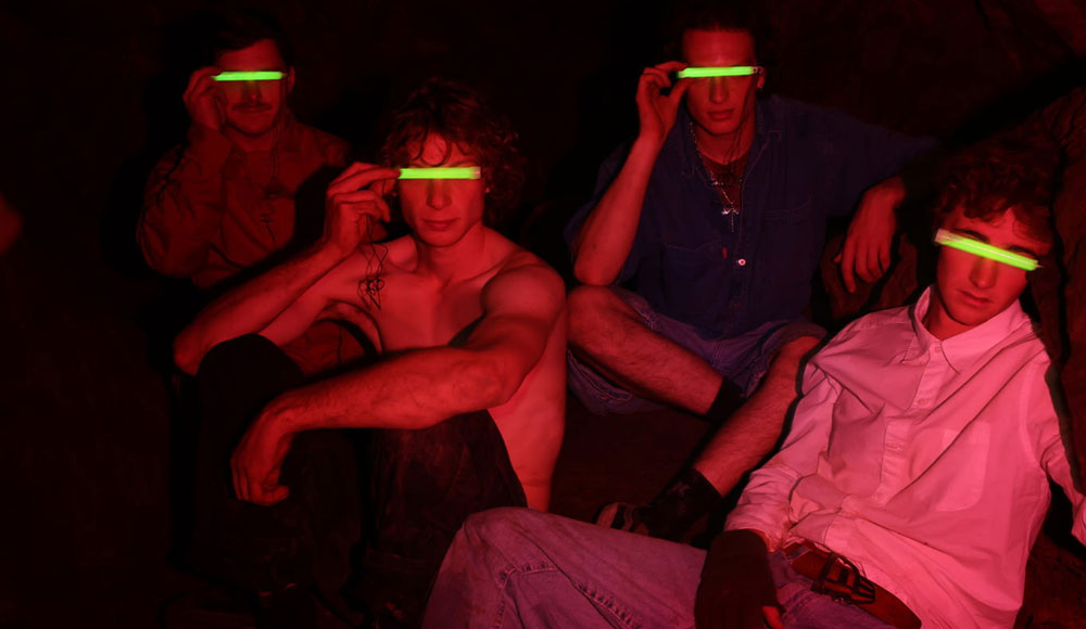 Members of the Santa Cruz band Red 40 pose under red lighting while holding glowing green strips over their eyes.