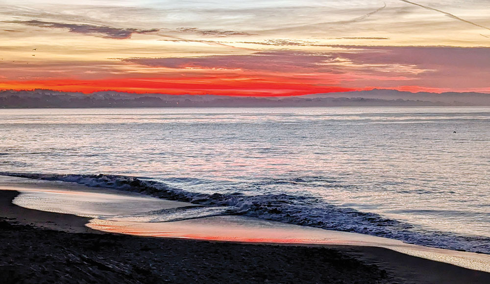 Waves roll onto a Santa Cruz beach at sunset beneath a streaked winter sky.
