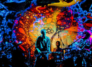 Shoegaze Redux Band members perform on stage in front of colorful, swirling psychedelic projections.