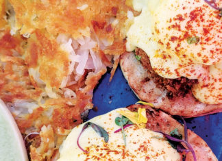 Come and Get It Crab cake Benedict served with poached eggs, hollandaise sauce, and crispy hash browns on a blue plate.
