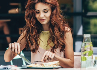 Dining Solo? A woman sits at a table cutting food on a plate during a solo meal.