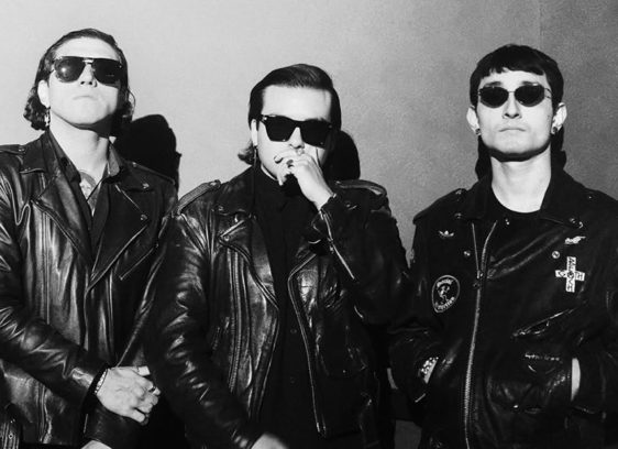 Things to do in Santa Cruz Three musicians wearing black leather jackets and sunglasses pose for a black-and-white portrait.