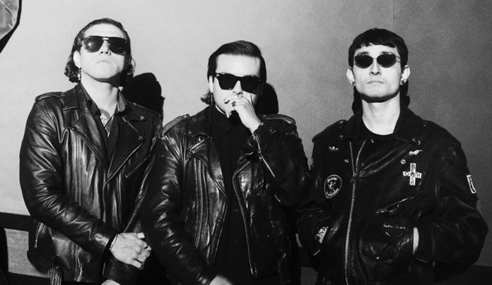 Things to do in Santa Cruz Three musicians wearing black leather jackets and sunglasses pose for a black-and-white portrait.