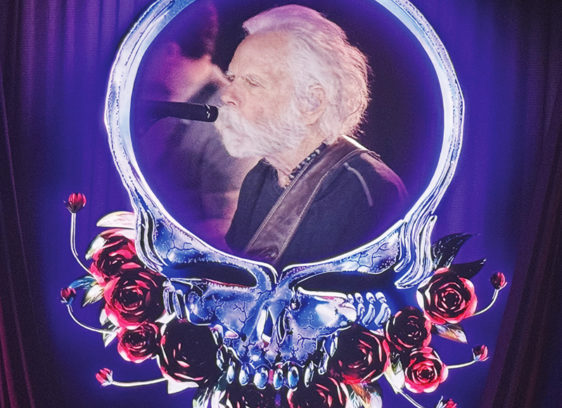 One More River to Cross An older Bob Weir sings into a microphone, framed by a glowing skull-and-roses stage graphic.