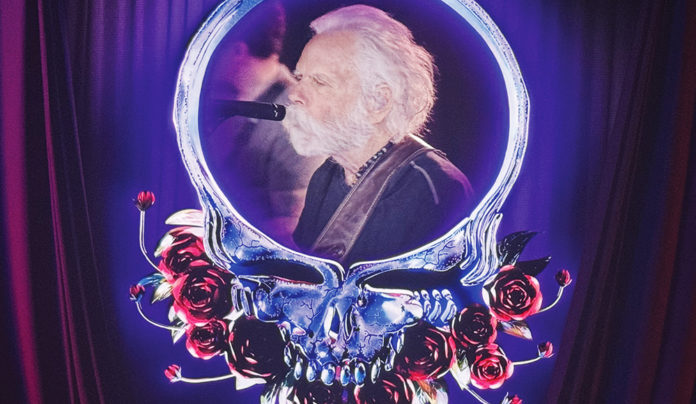 One More River to Cross An older Bob Weir sings into a microphone, framed by a glowing skull-and-roses stage graphic.