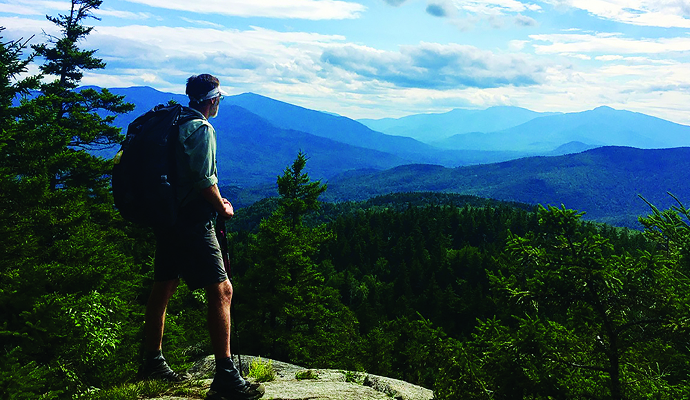 Hiker looks out over forested mountains during a long-distance trek