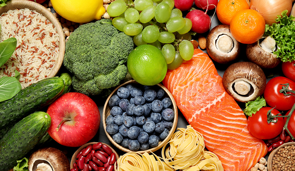 Fresh fruits, vegetables, grains, legumes, and salmon arranged on a table.
