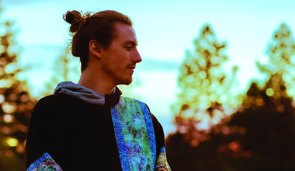 DJ Neumonic seen in profile with trees and ocean in the background.