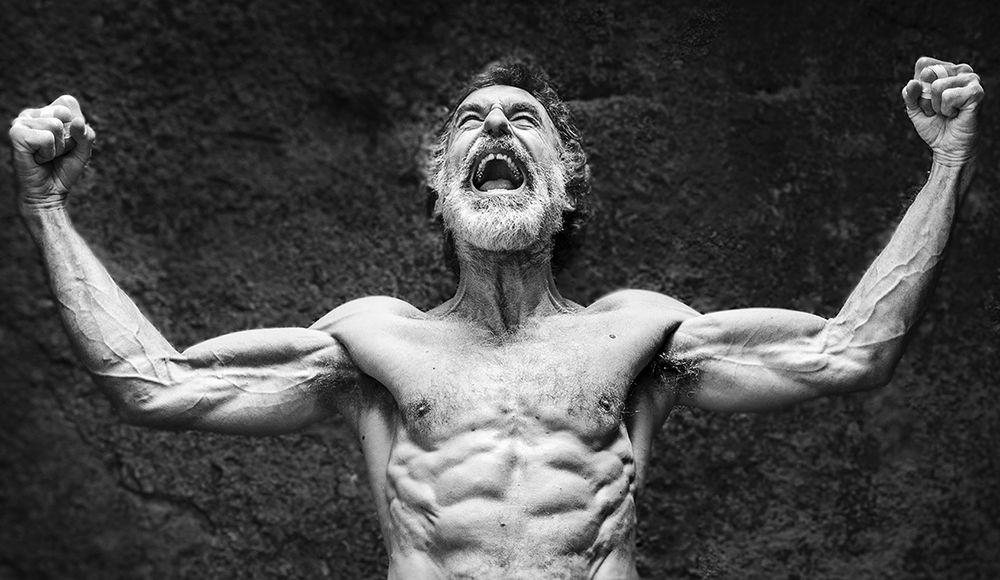 An older climber flexes his arms in a dramatic black-and-white portrait from Old Man Lightning.