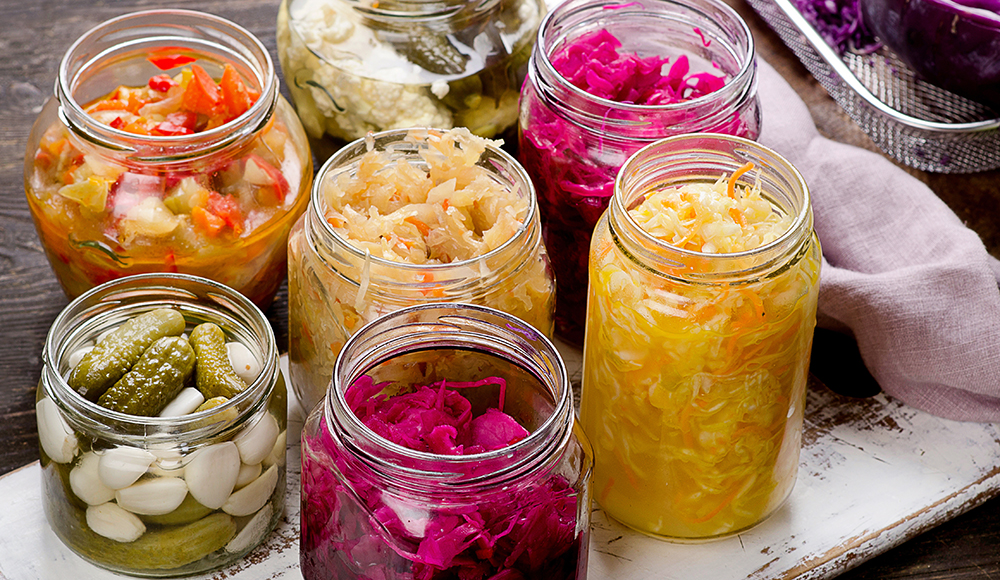 Jars of fermented vegetables including sauerkraut, pickles, and colorful cabbage on a rustic table