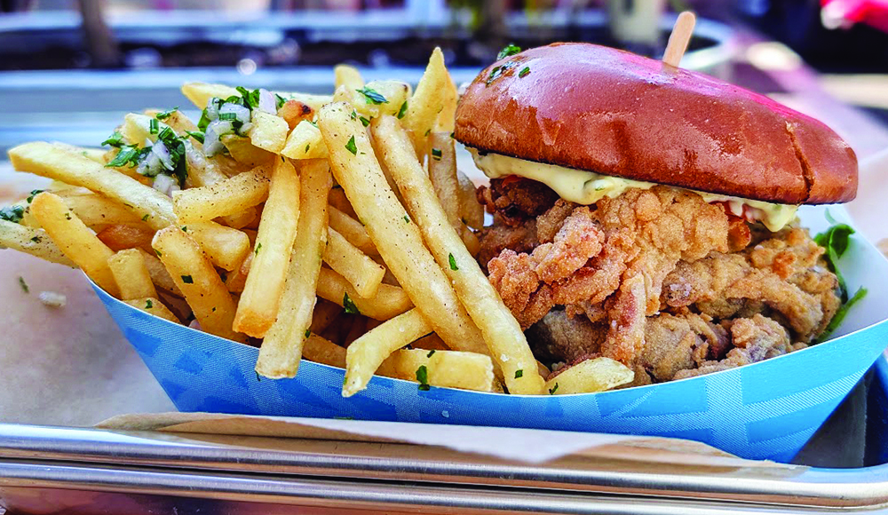Fried chicken sandwich on a brioche bun served with seasoned French fries in a paper tray