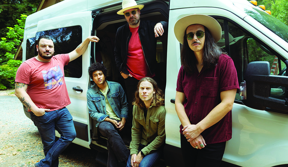 The Coffis Brothers standing outside their tour van in a wooded setting