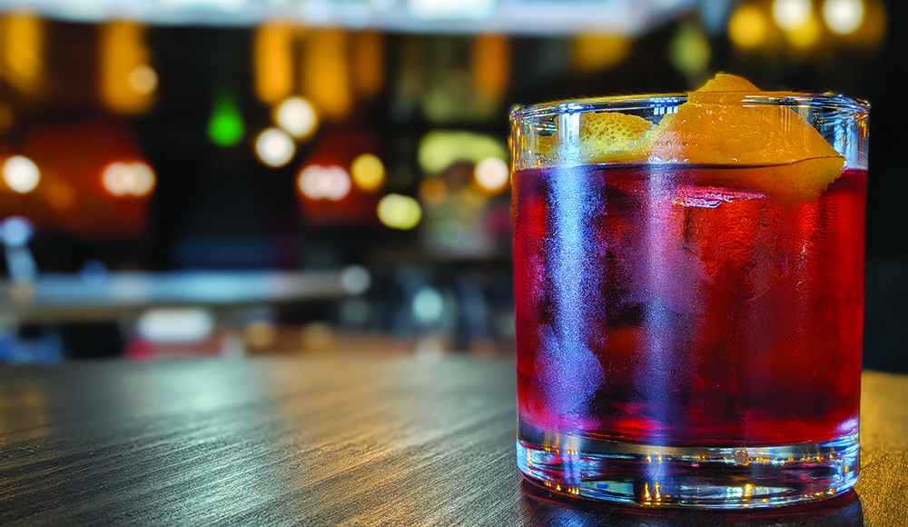 Red cocktail with orange peel garnish on bar at The Hotel Santa Cruz