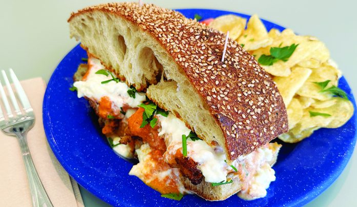Brew Chew Chicken parmesan sandwich with melted cheese and chips on blue plate