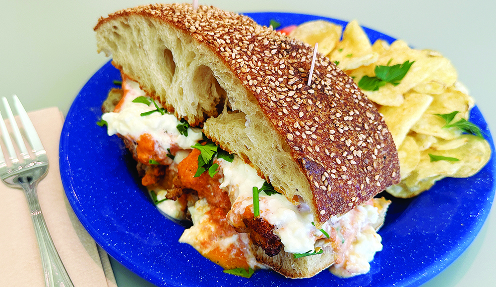 Chicken parmesan sandwich with melted cheese and chips on blue plate