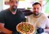 Melded and Melted Two men holding a Mexican-style pizza topped with chorizo jalapeños and cilantro at Originals Pizza