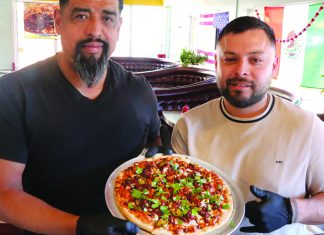 Melded and Melted Two men holding a Mexican-style pizza topped with chorizo jalapeños and cilantro at Originals Pizza