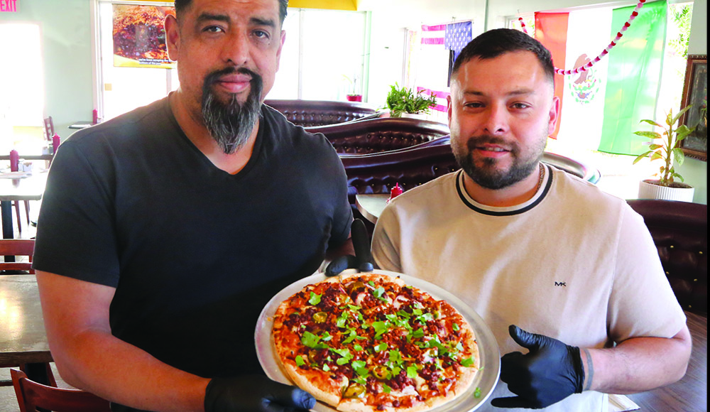 Two men holding a Mexican-style pizza topped with chorizo jalapeños and cilantro at Originals Pizza