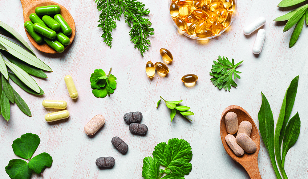 Various herbal supplements and capsules with green leaves on table