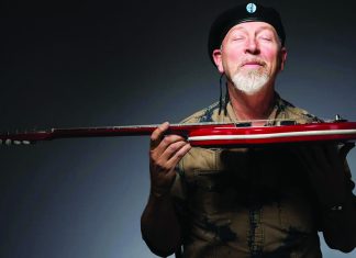 Playing Live Man holding red electric guitar wearing black beret smiling with eyes closed