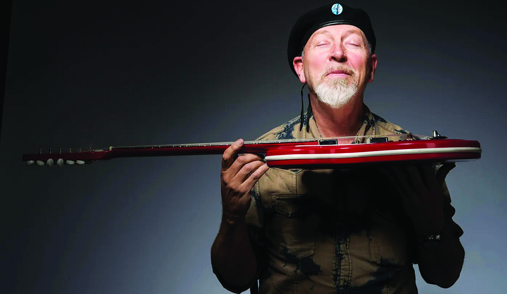Man holding red electric guitar wearing black beret smiling with eyes closed