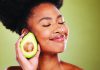 Make Your Skin Glow Woman smiling with eyes closed holding half an avocado near her face