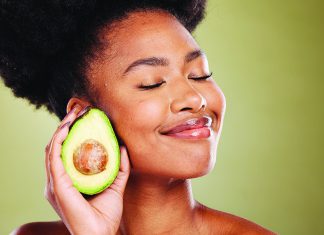 Make Your Skin Glow Woman smiling with eyes closed holding half an avocado near her face
