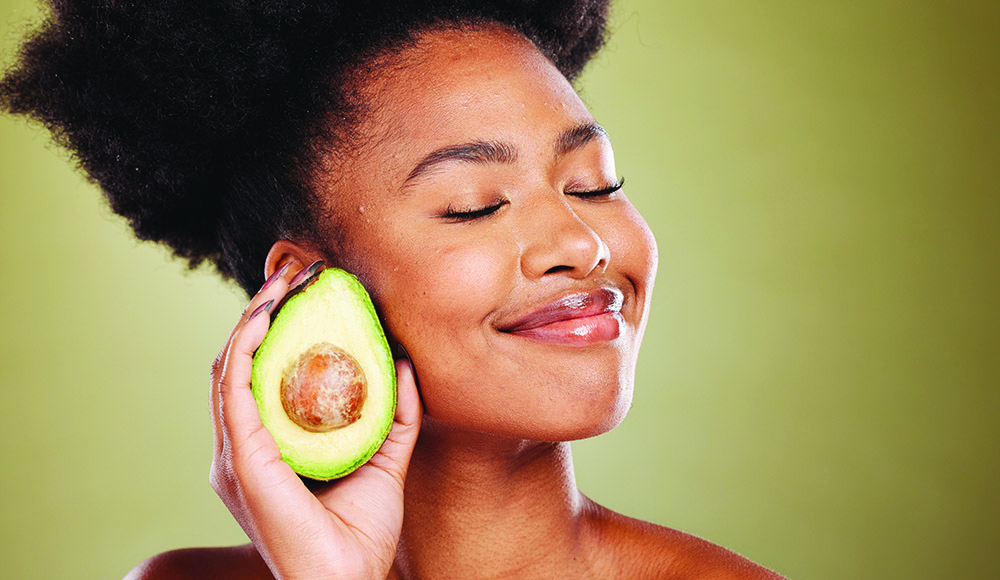 Woman smiling with eyes closed holding half an avocado near her face