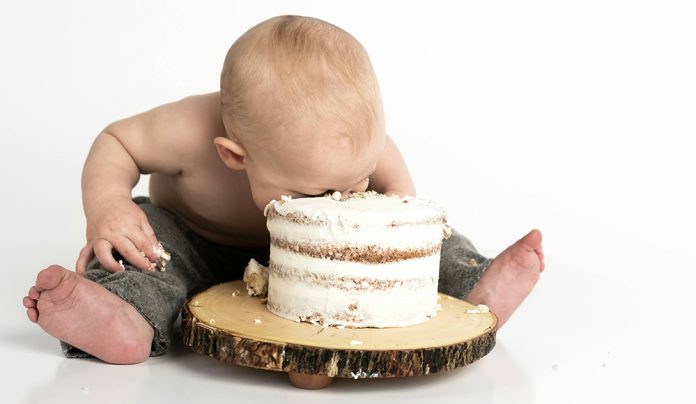 Baby Foodย Baby smashing face into small frosted cake on wooden stand