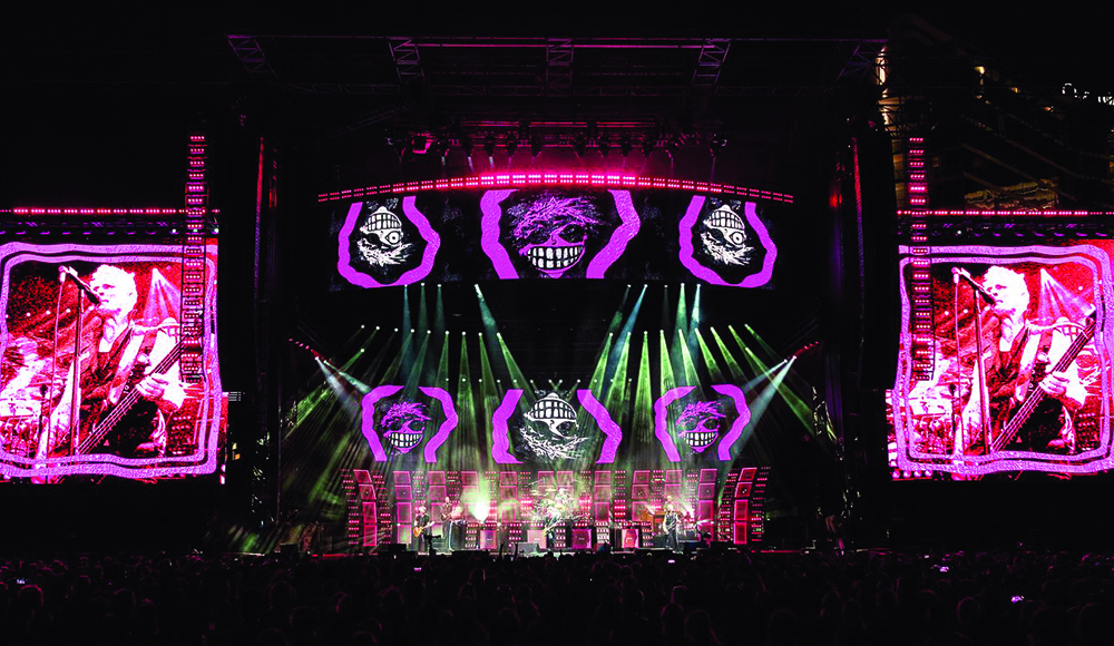Green Day performing on large concert stage with bright LED screens and visuals