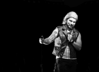 Send in the Lagoonies Black-and-white photo of a stand-up comedian in a leather vest holding a microphone on stage at Blue Lagoon in Santa Cruz