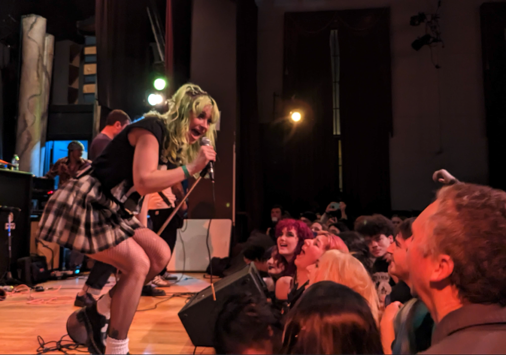 Kat Moss of Scowl performing live, singing into microphone with crowd at Santa Cruz show