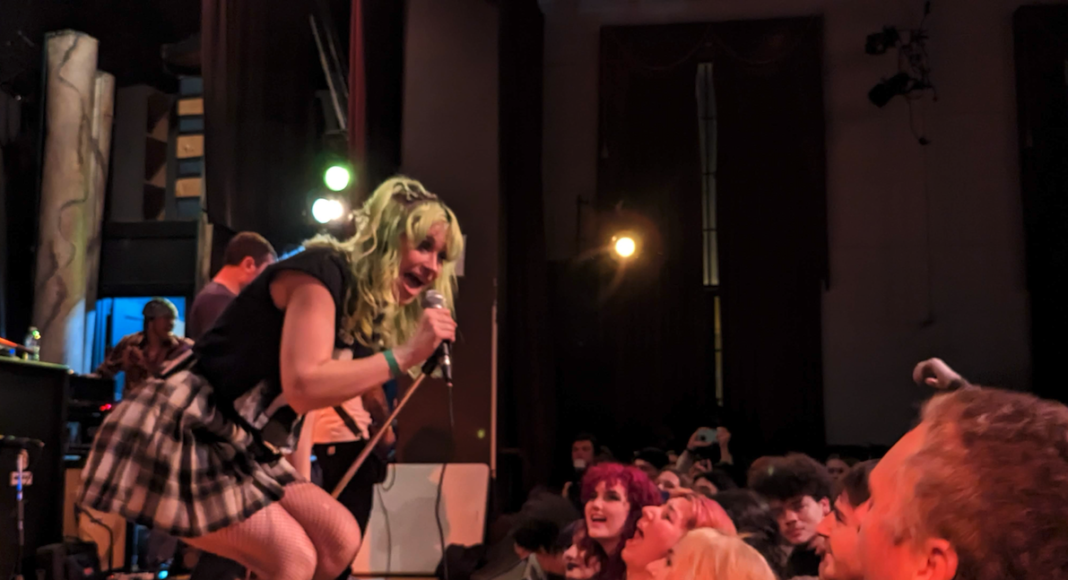 Kat Moss of Scowl performing live, singing into microphone with crowd at Santa Cruz show