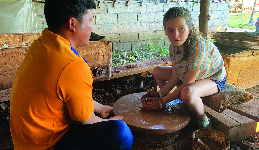 Child learning pottery on traditional wheel in Laos during family travel