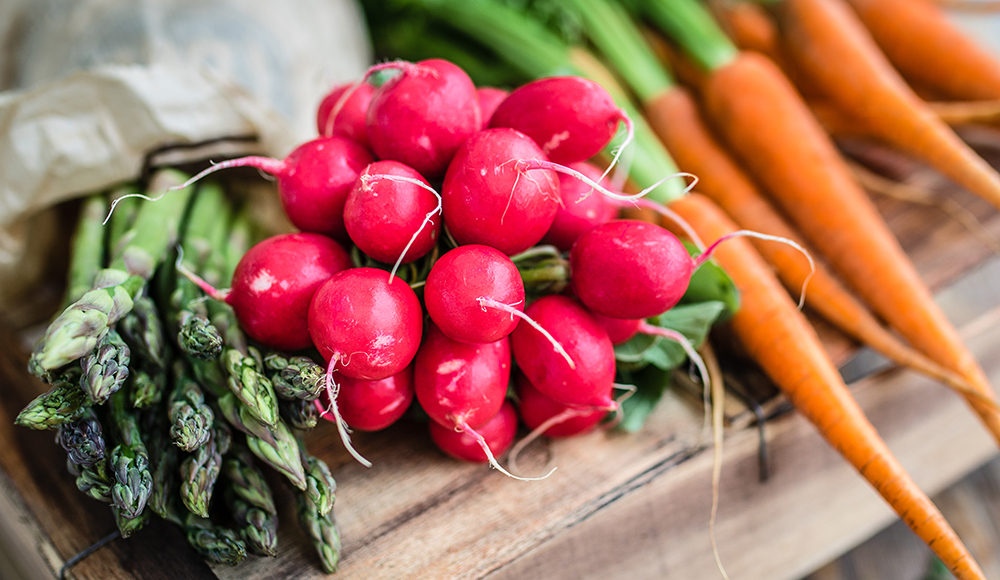 Fresh spring vegetables including radishes, asparagus and carrots on a wooden surface