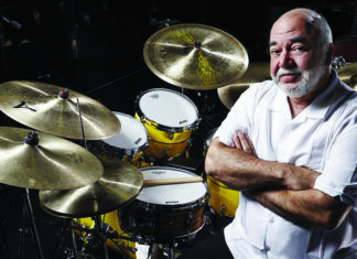 Things to do in Santa Cruz Drummer Peter Erskine sits beside a drum kit with cymbals.
