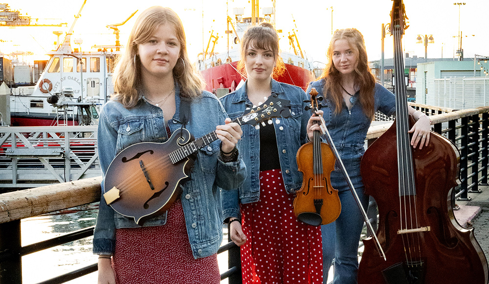Members of bluegrass trio Sweet Sally pose with mandolin, fiddle and upright bass.