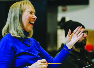 Tragedy Into Art Choral director Cheryl Anderson smiles and gestures during a rehearsal.