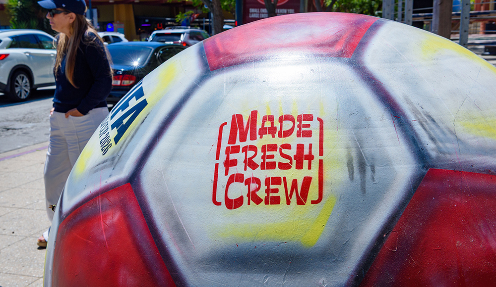 Close-up of a giant painted FIFA World Cup 2026 soccer ball featuring the Made Fresh Crew logo in downtown Santa Cruz.