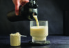 Protein Obsession Protein drink being poured into a glass beside a scoop of protein powder.