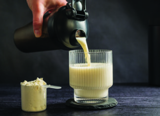 Protein Obsession Protein drink being poured into a glass beside a scoop of protein powder.