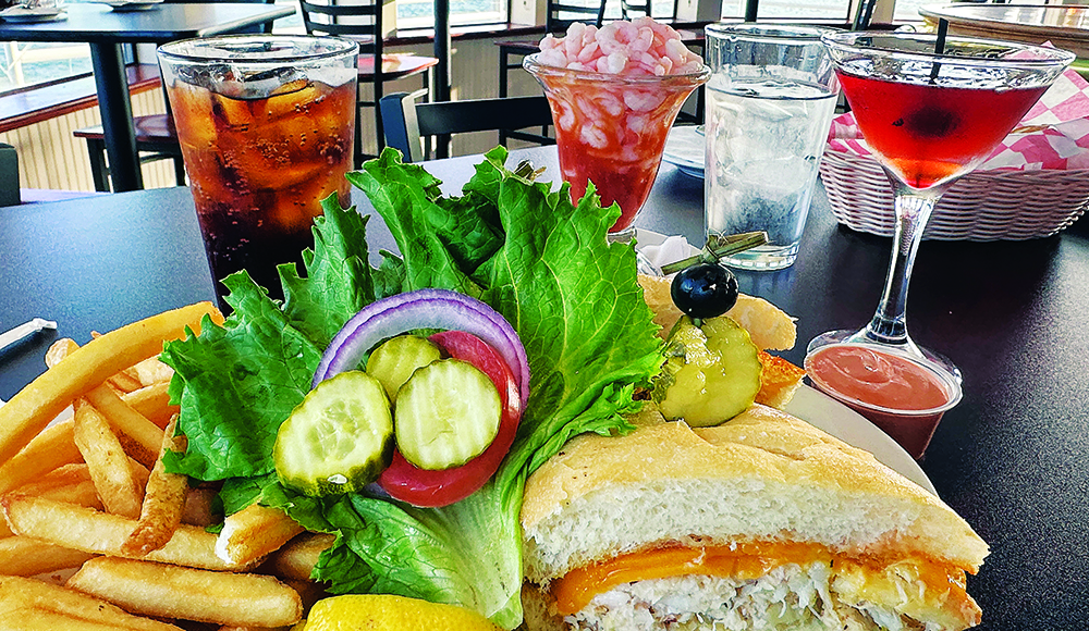 Crab melt sandwich, fries, shrimp cocktail and cocktails on a table overlooking Monterey Bay at Stagnaro Brothers Seafood Restaurant.